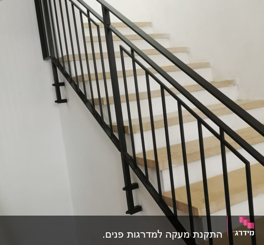 מעקה מתכת שחור על מדרגות עץ בהירות